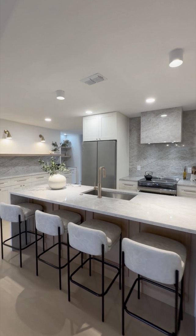 Kitchen remodel in Tampa, FL with a long stone island, slab backsplash and a plaster range hood